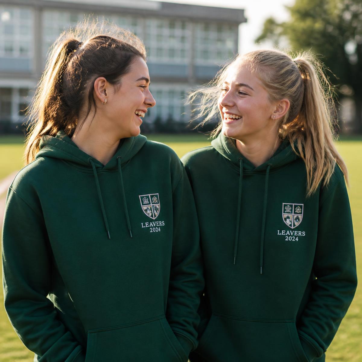 Two school leavers wearing bottle green hoodies with a printed school badge
